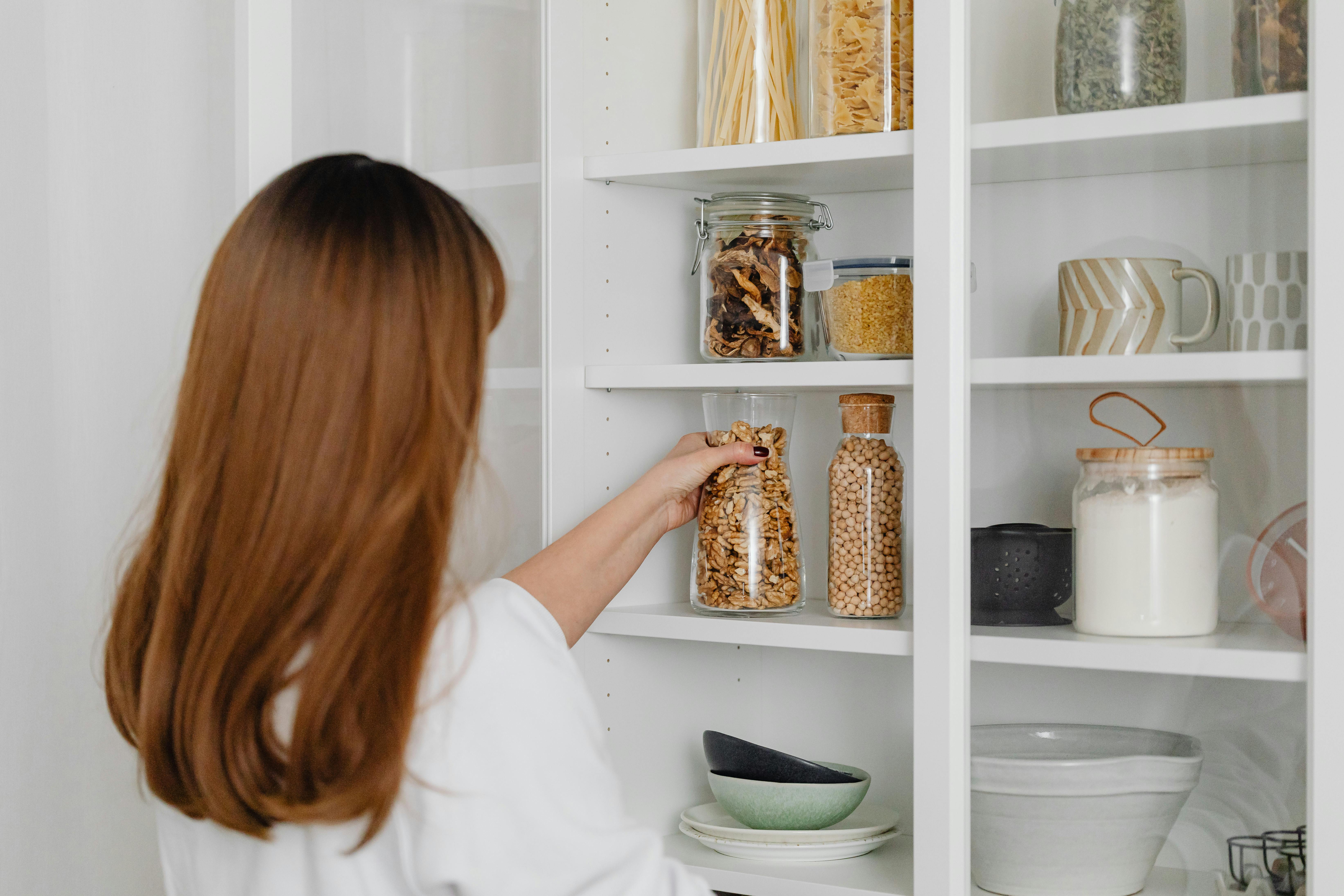 Woman packing a jar of peanuts onto a clean and organized kitchen shelf